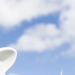 a hand putting a coin into a piggy bank against a blue sky