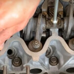 a hand reaching into an engine to adjust the tappets
