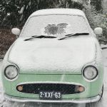 A Figaro car with a dusting of snow with the windscreen showing a christmas decoration