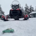 a model Figaro car in the snow in front of a snow mobile