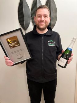Marios standing holding the award for The Figaro Shop and a bottle of champagne