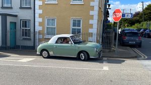 A green Figaro parked by the side of a road