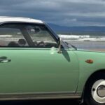 A green Figaro parked on a beach looking out to sea